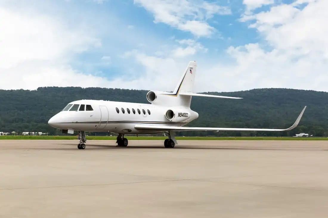 A Falcon jet sits on the tarmac with mountains in the background.