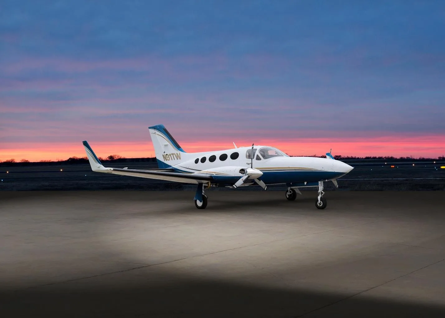 A white and blue Cessna 414 Chancellor (N91TW) parked on an airfield at sunset.