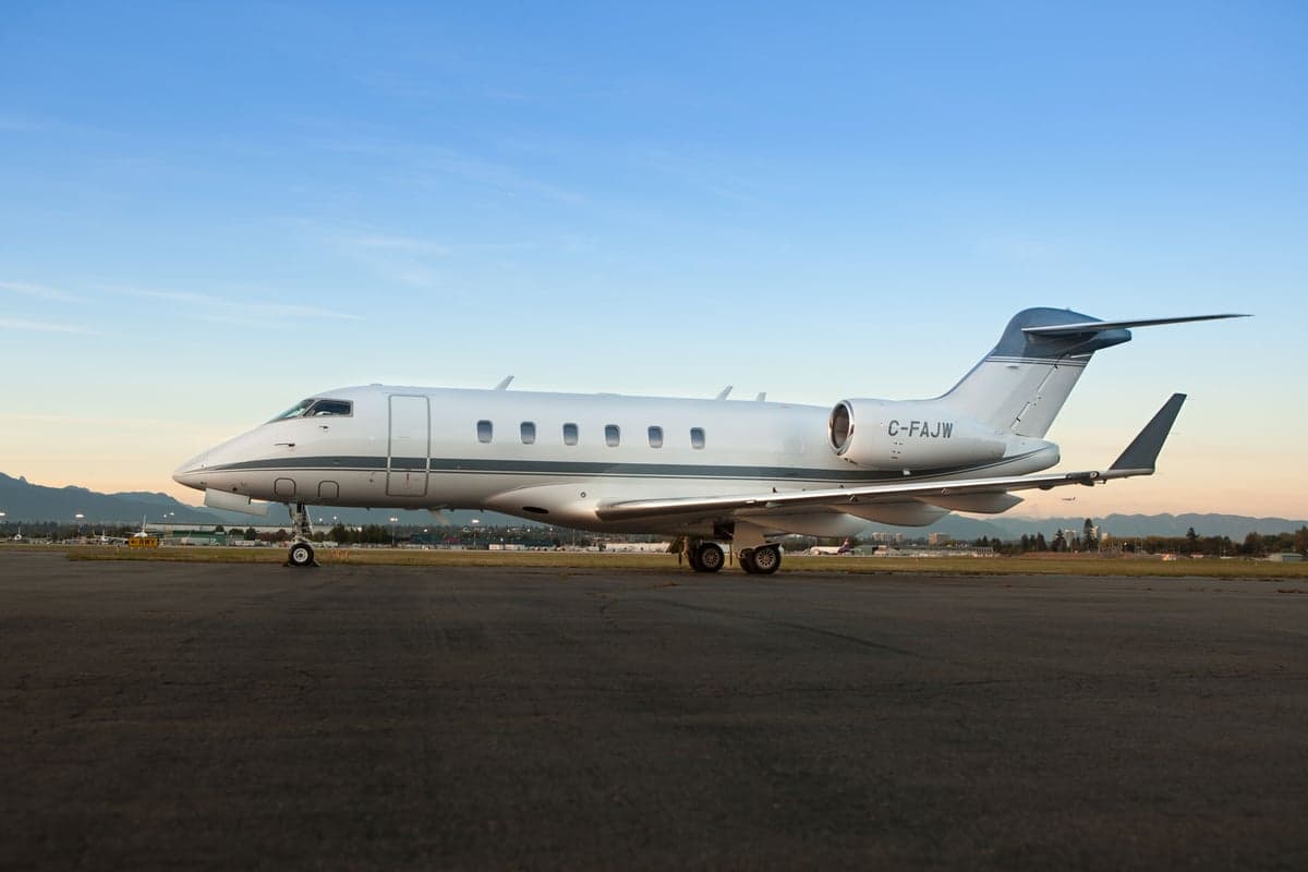 A Bombardier Challenger 350 business jet with registration C-FAJW is parked on the tarmac.