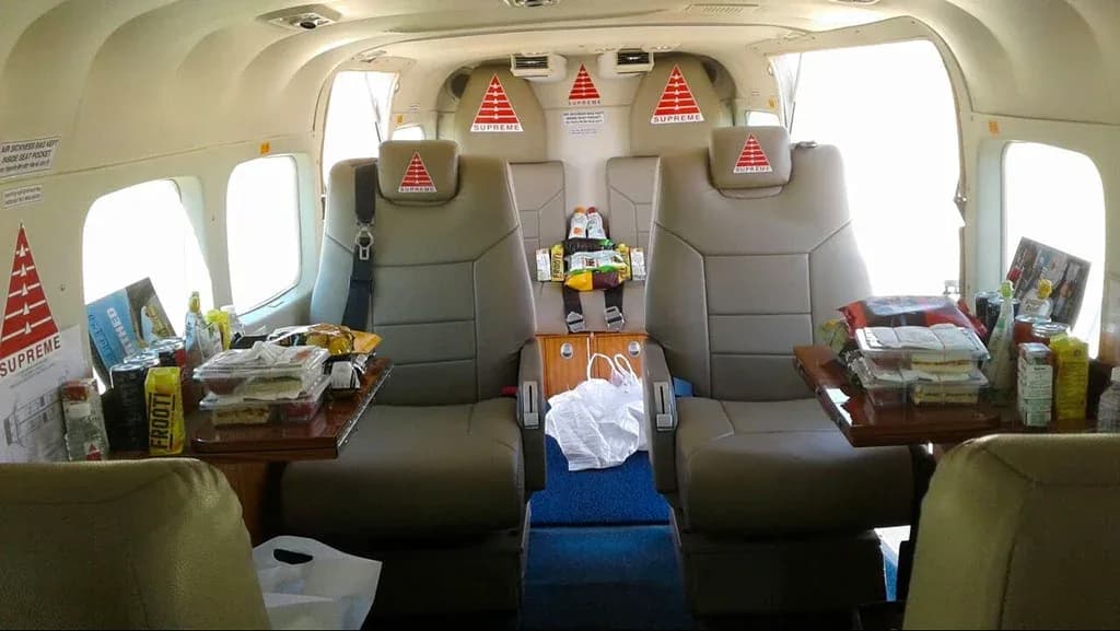A wider view of the aircraft's interior cabin, showing tan seats, tables with snacks, and a blue carpeted aisle.