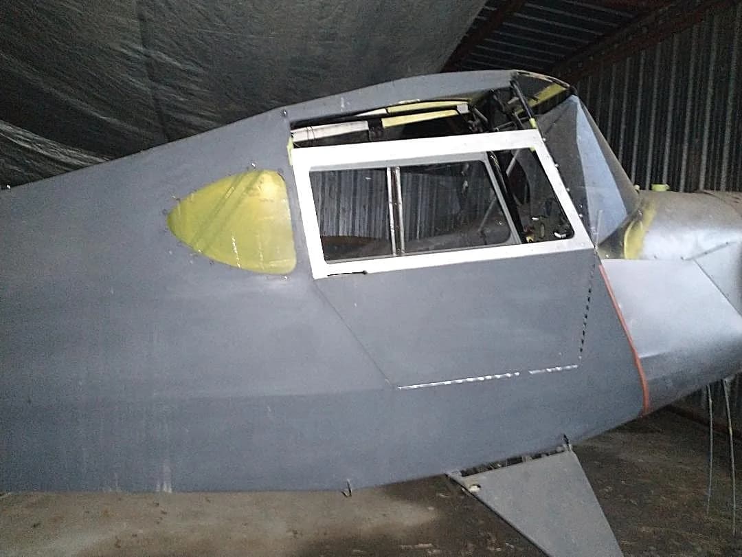 A close-up of the grey-primed fuselage and cockpit windows of an aircraft under construction.