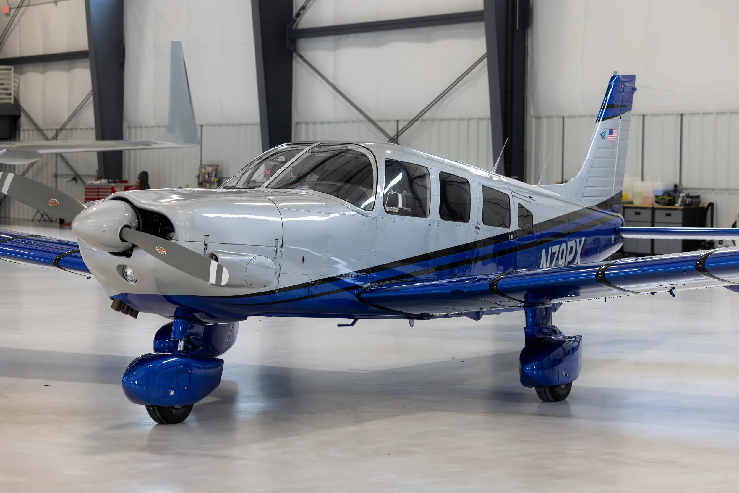 Front quarter view of a silver and blue Piper PA-28 Cherokee aircraft with registration N70PX inside a hangar.