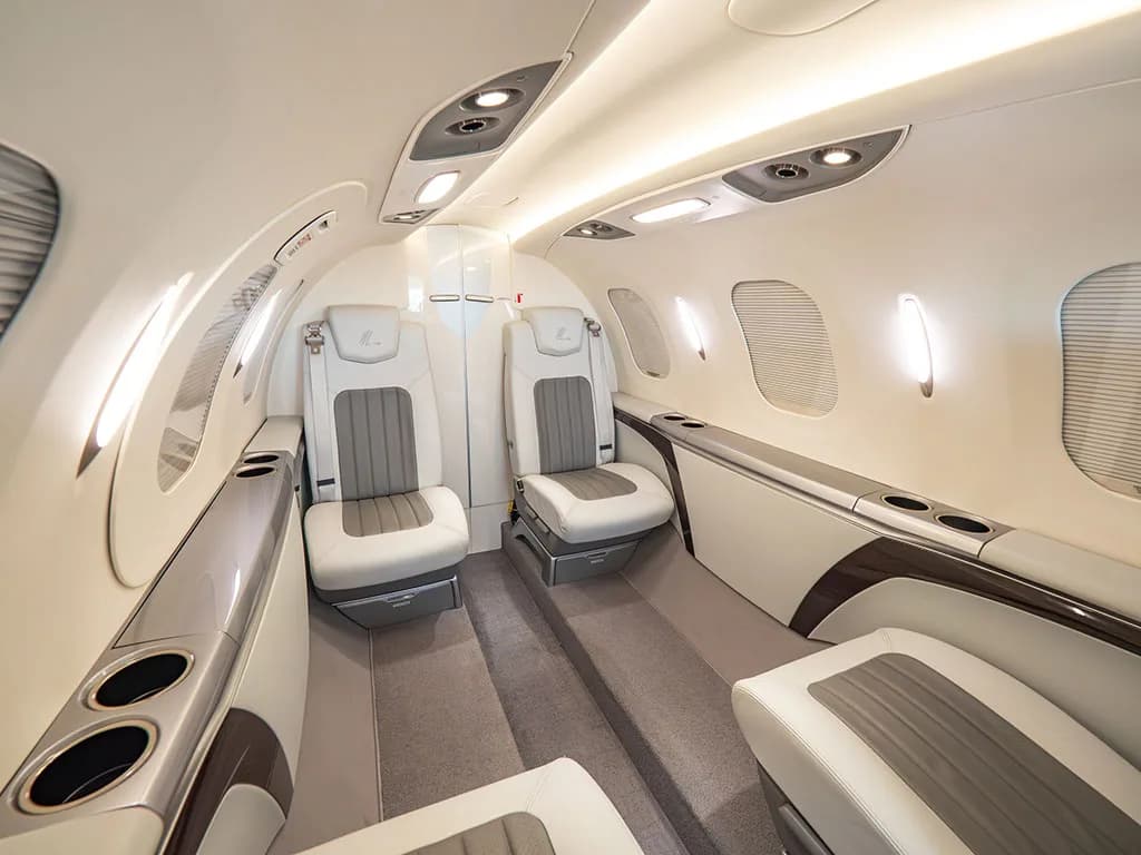 A slightly angled view of the HondaJet's interior cabin with light grey and white leather seats and overhead lighting.