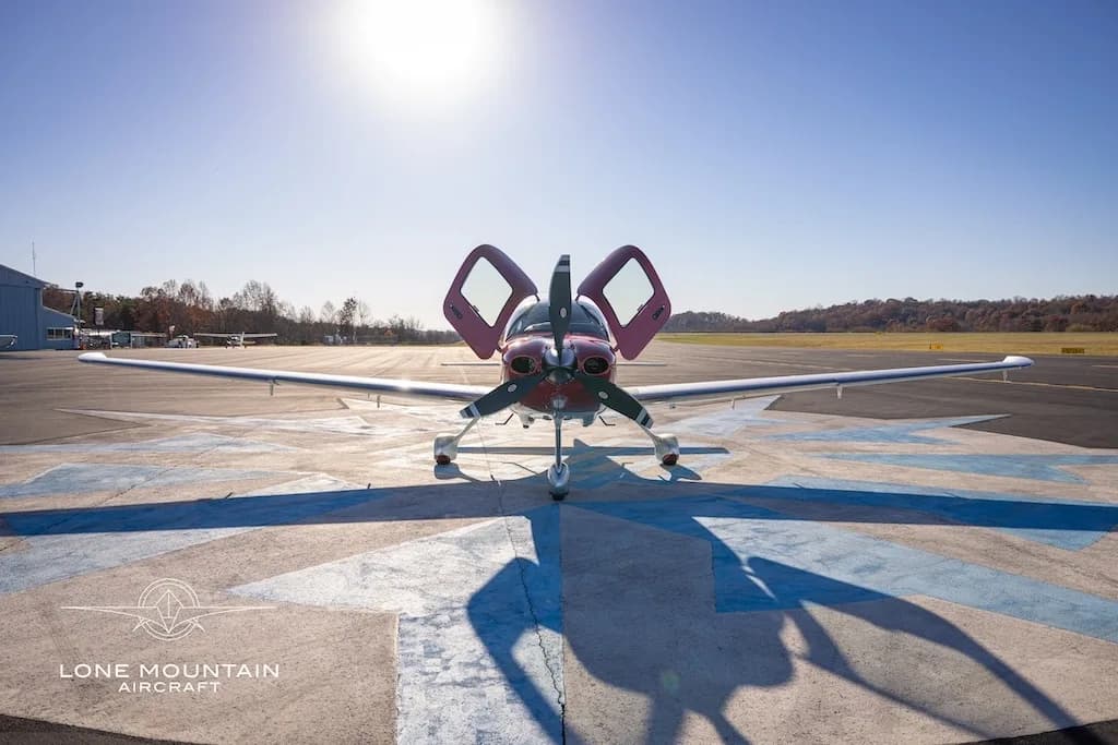 A front view of a red and white Cirrus SR22 aircraft with registration N5785C parked on an airfield with its doors open.