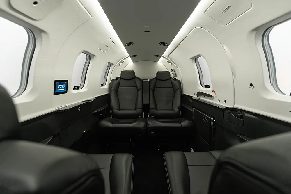 A clean, modern private jet cabin with black leather seats and white walls, viewed from the front.