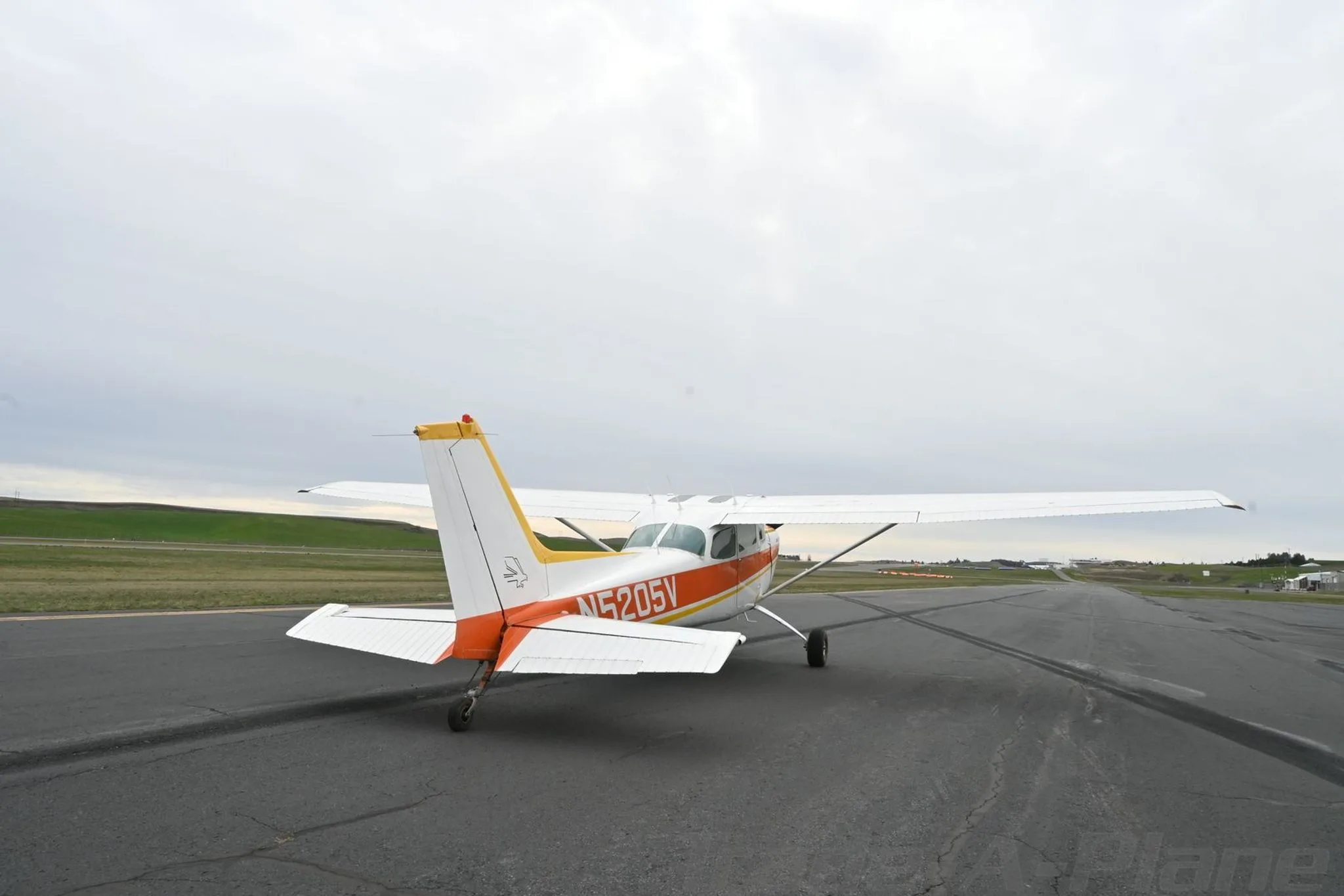A white and orange Cessna 172 Hawk XP II (N5205V) parked on an airfield, viewed from the rear-left side.