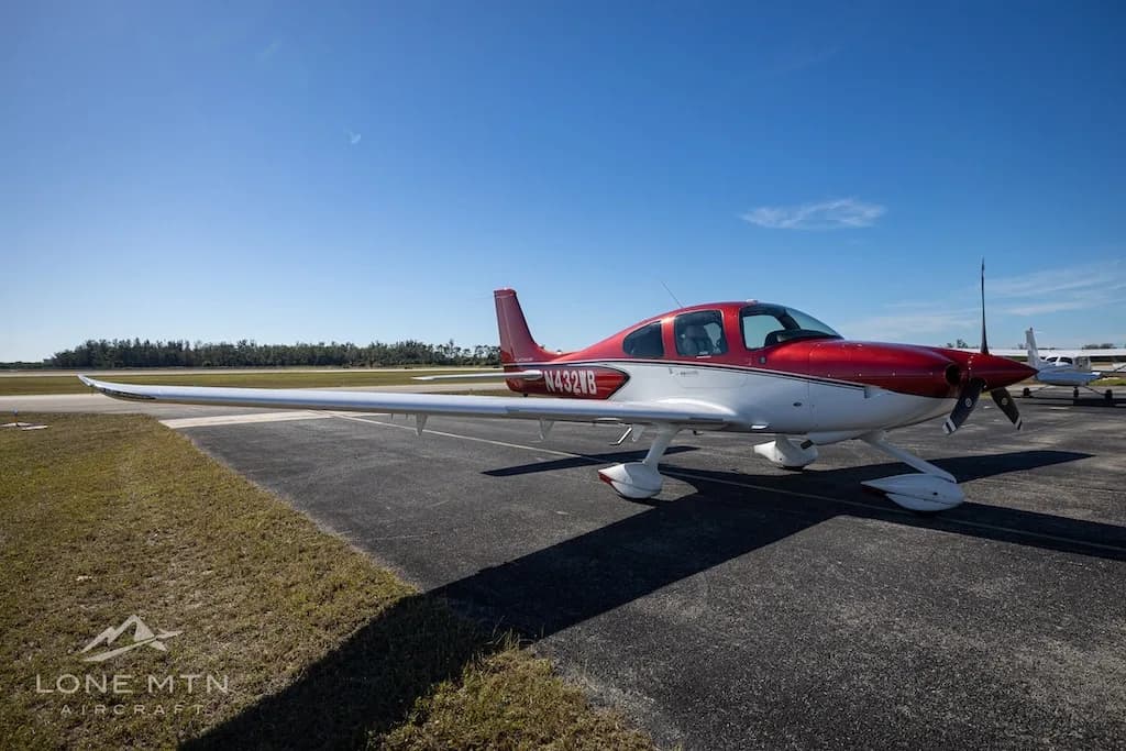 A red and white Cirrus SR20 aircraft (N432WB) parked on an airport tarmac under a clear blue sky.