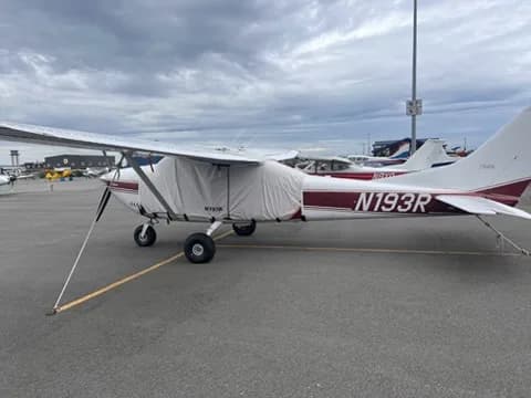 A white and maroon Cessna 182 aircraft (N193R) with a protective cover over its front section, parked on an tarmac.