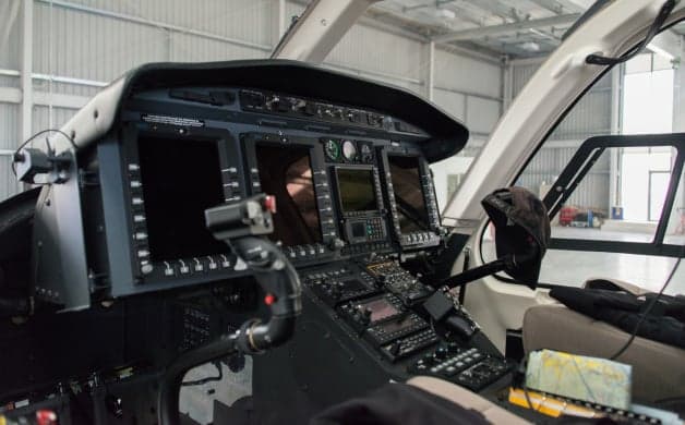 The cockpit of a helicopter with a view of a vineyard.
