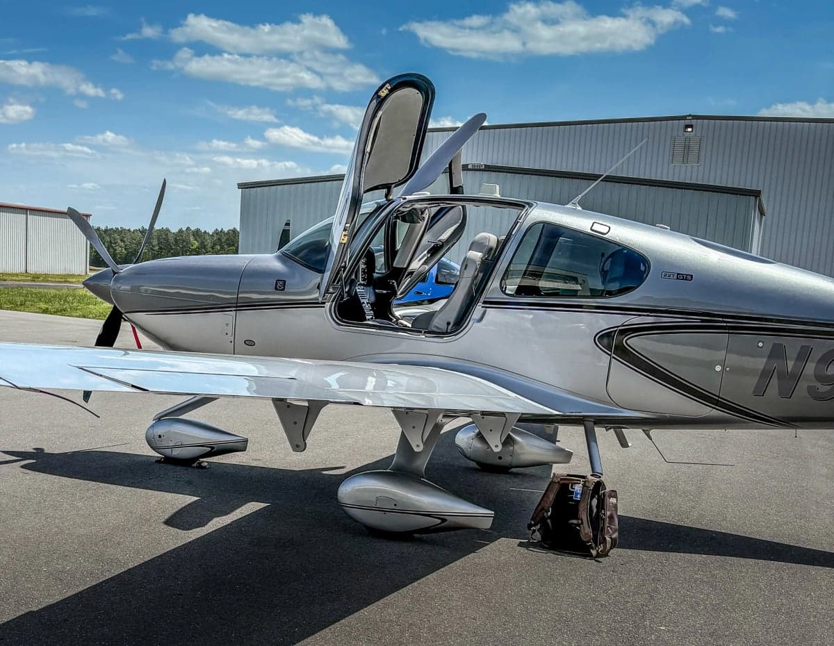 A Cirrus SR22T aircraft is parked on the tarmac with its gull-wing doors open.