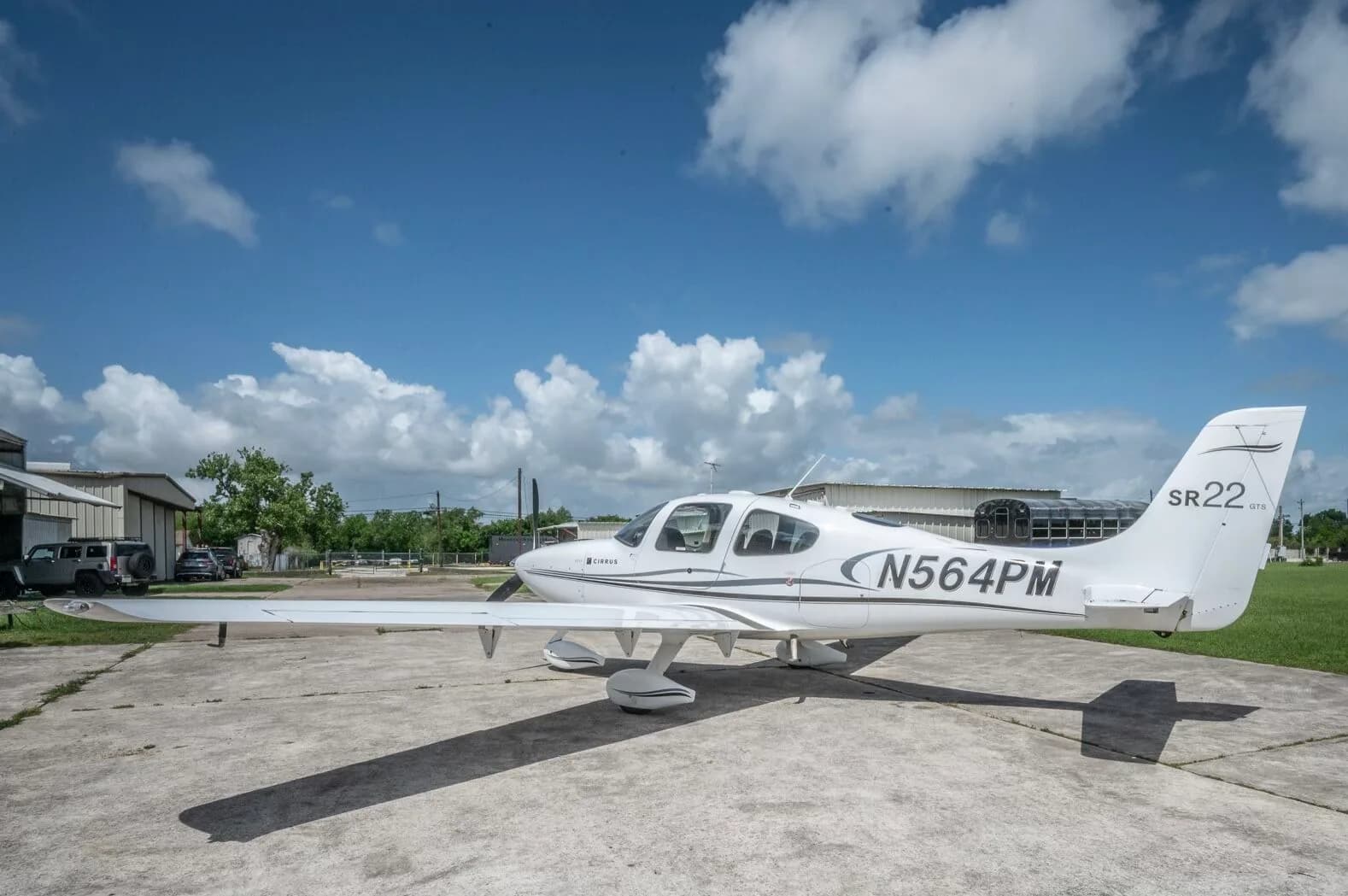 A side view of a white Cirrus SR22 GTS aircraft with N564PM registration parked on a concrete ramp.