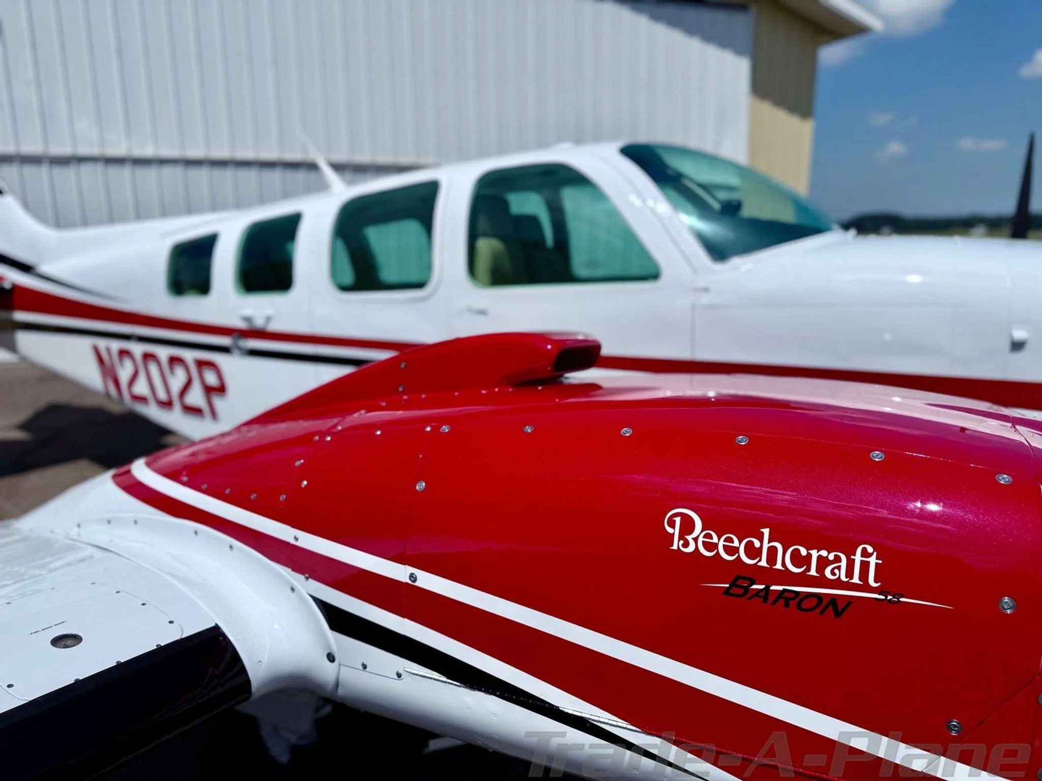 Close-up of the red engine cowling with "Beechcraft BARON" logo and the white fuselage of N202P in the background.