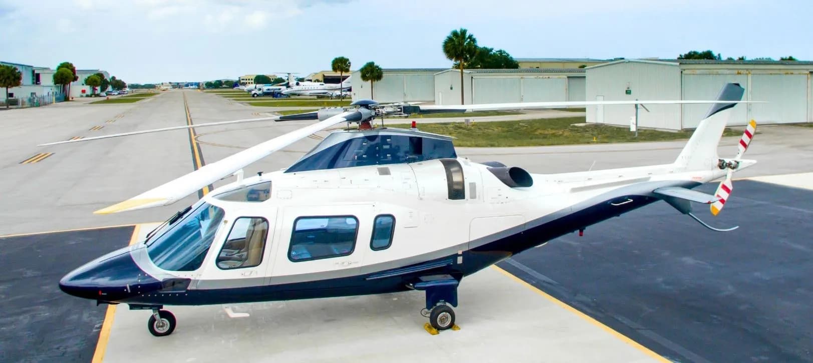 A white and blue AgustaWestland AW109 helicopter on the tarmac.