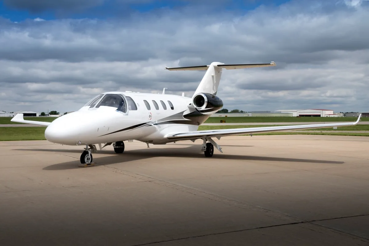 A white private jet with black and grey accents parked on an airfield under a cloudy sky.