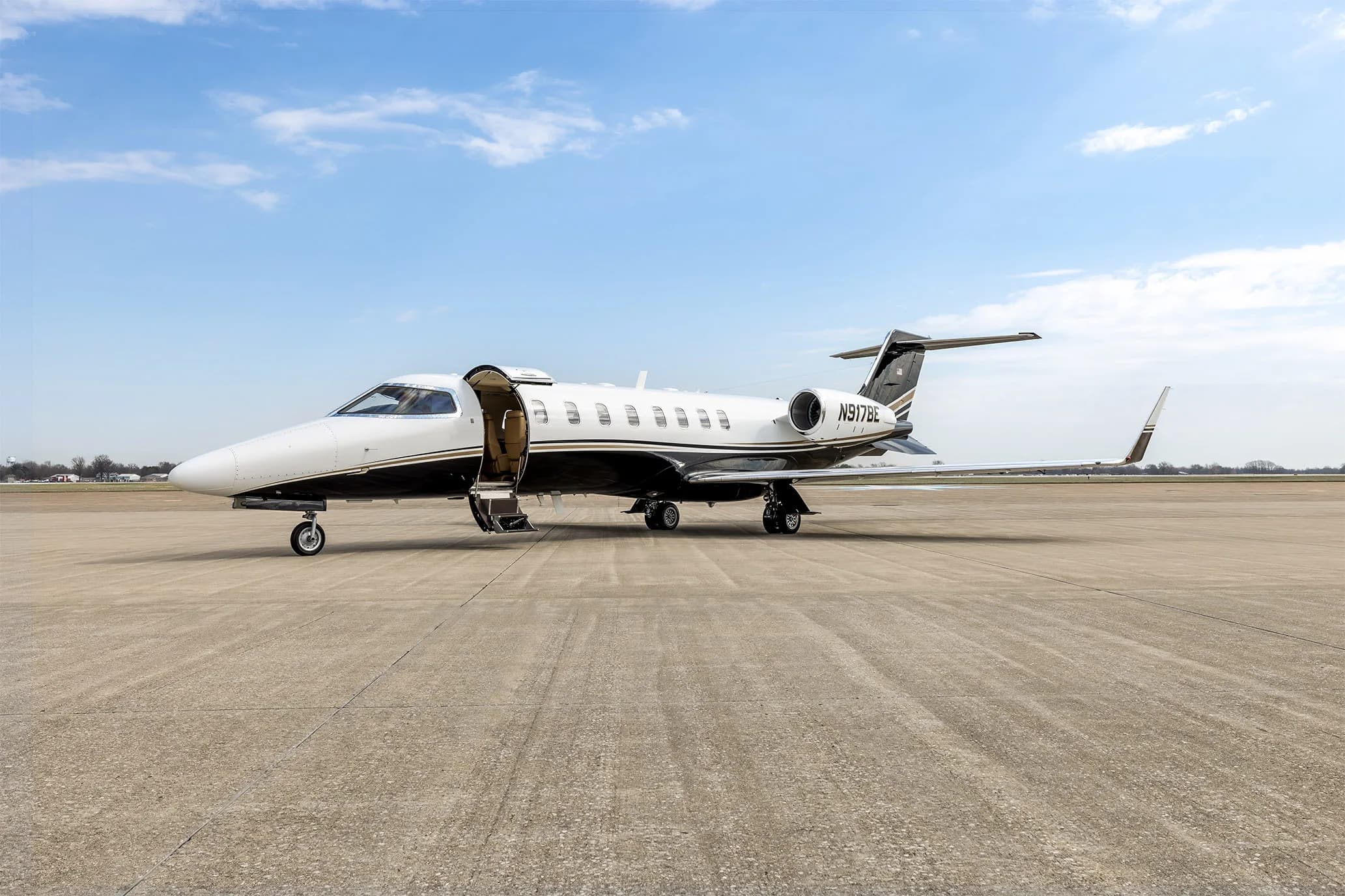 A Learjet 60 business jet with its main cabin door open and stairs extended, parked on an airfield.