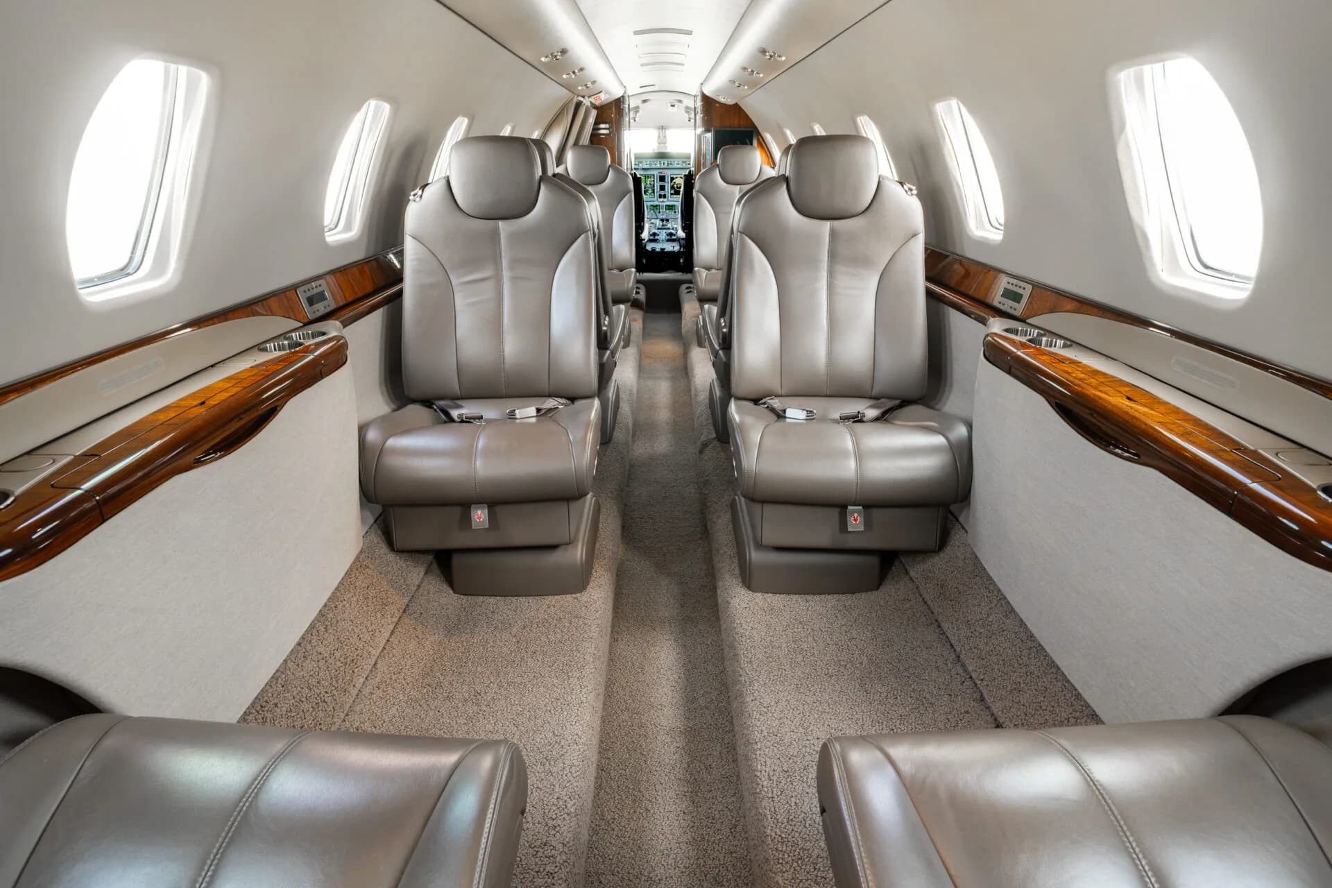 The luxurious cabin interior of a business jet with tan leather seats and polished wood accents.