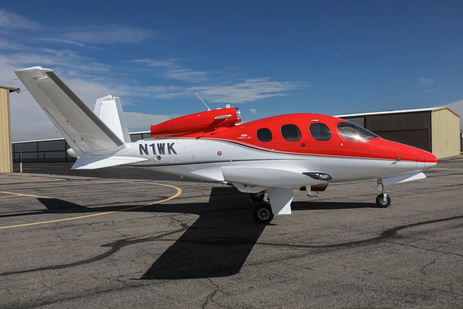 A red and white Cirrus Vision Jet (N1WK) parked on a tarmac, viewed from the side.