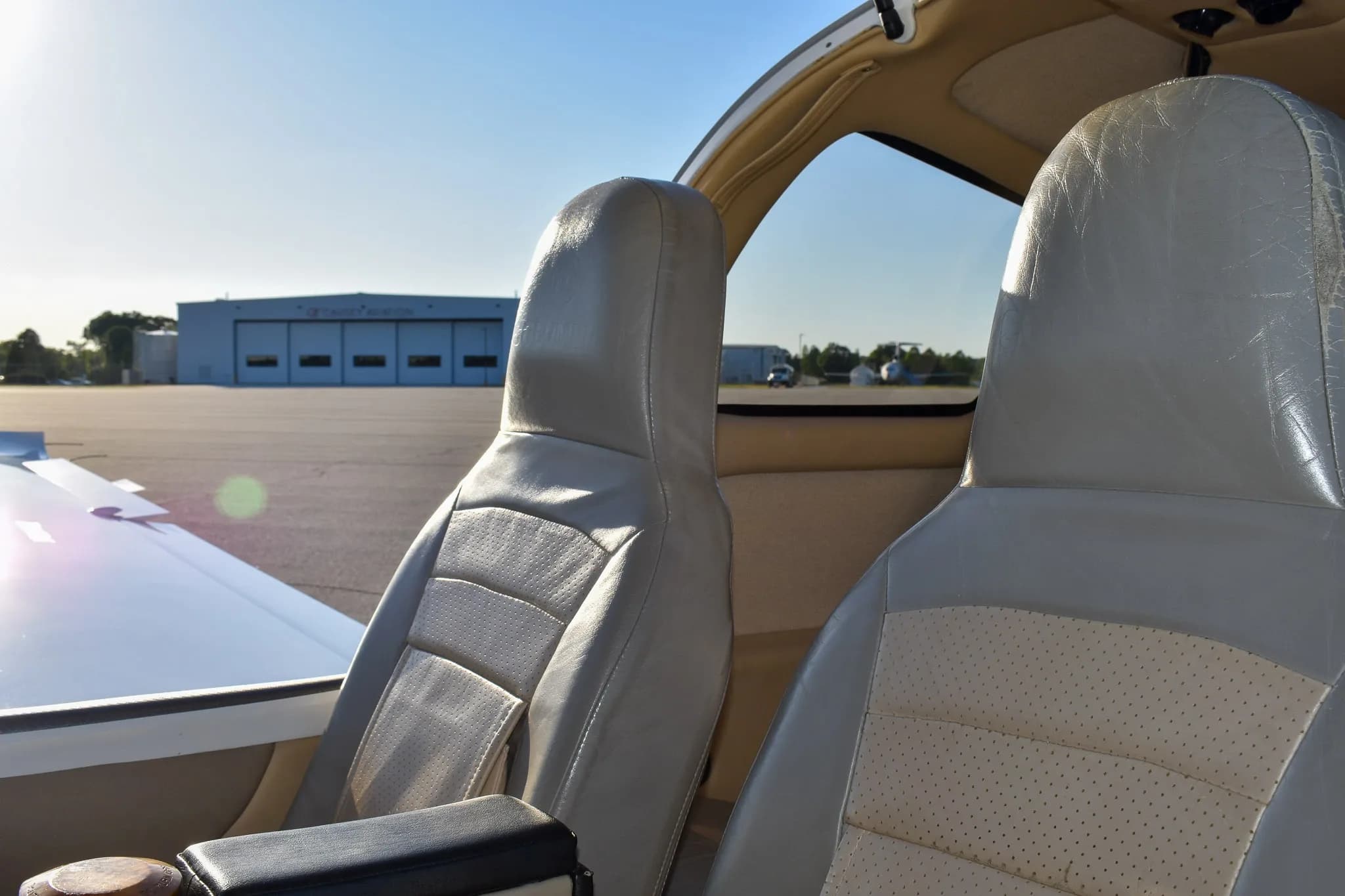 View from inside the aircraft cabin showing the front seats and a hangar in the background.