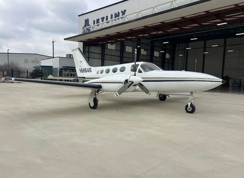 A white twin-engine Cessna 414 Chancellor with black and gold stripes, registration N68646, parked on an apron in front of a hangar.