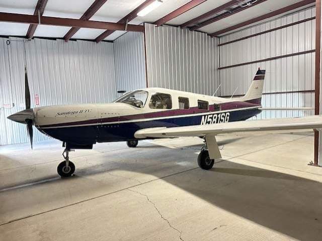 A blue, white, and purple Piper Saratoga II TC aircraft (N581SG) parked inside a hangar.