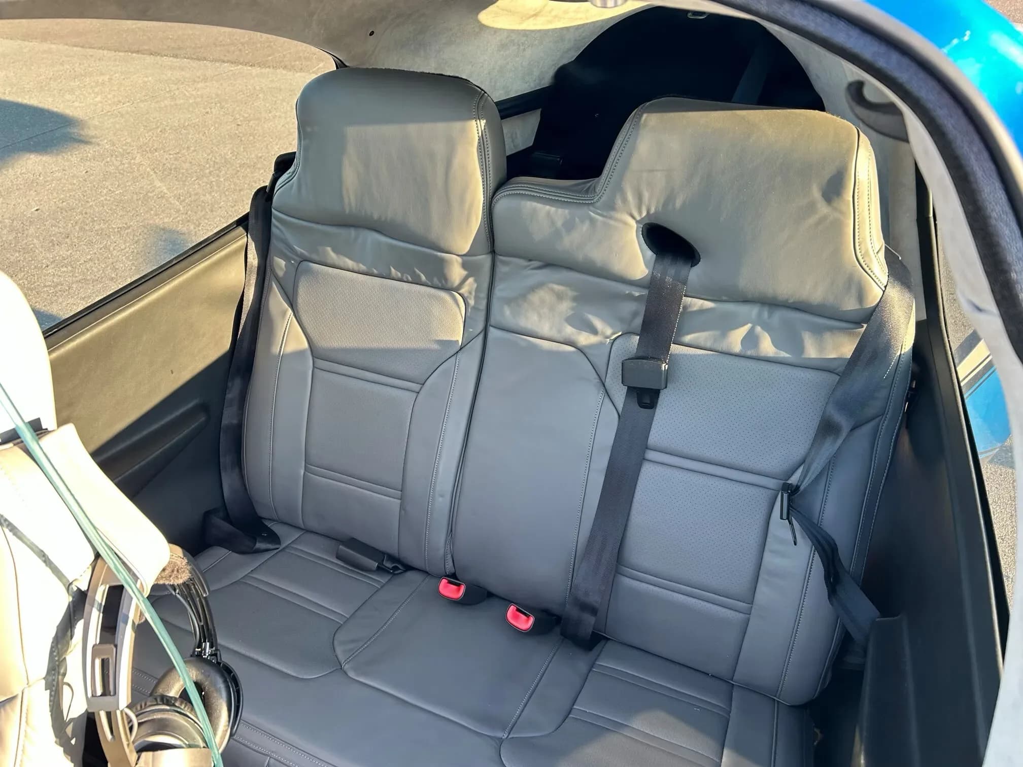 The gray leather rear bench seat of a Cirrus SR22 cabin with seatbelts.