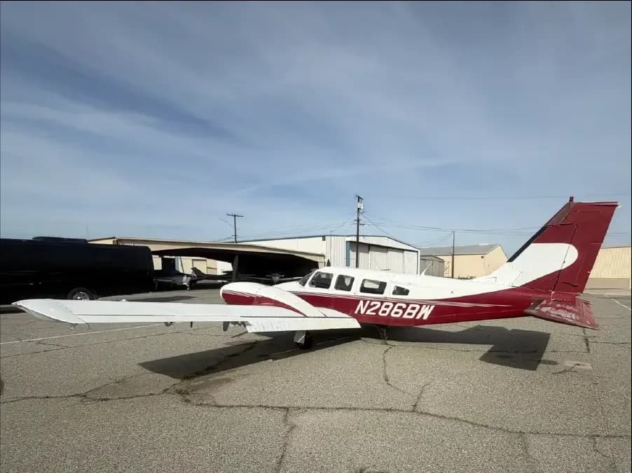 A white and red single-engine propeller aircraft, registration N286BW, parked on an asphalt apron with hangars in the background.