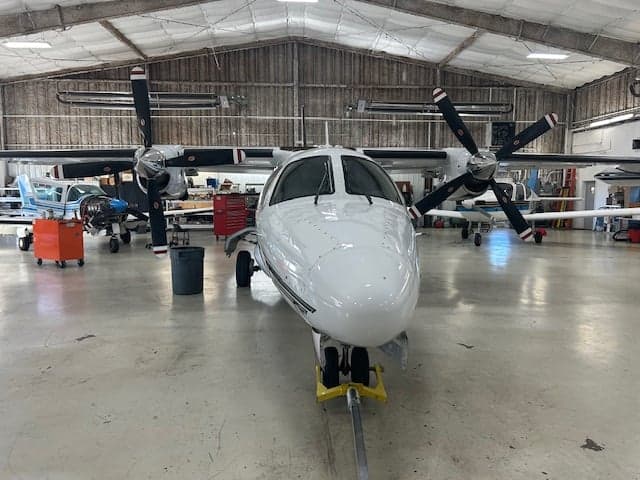 Front view of a white aircraft with black stripes inside a hangar.