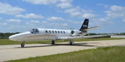 Side view of a white Cessna Citation CJ3 with black and gold accents parked on an airport tarmac.