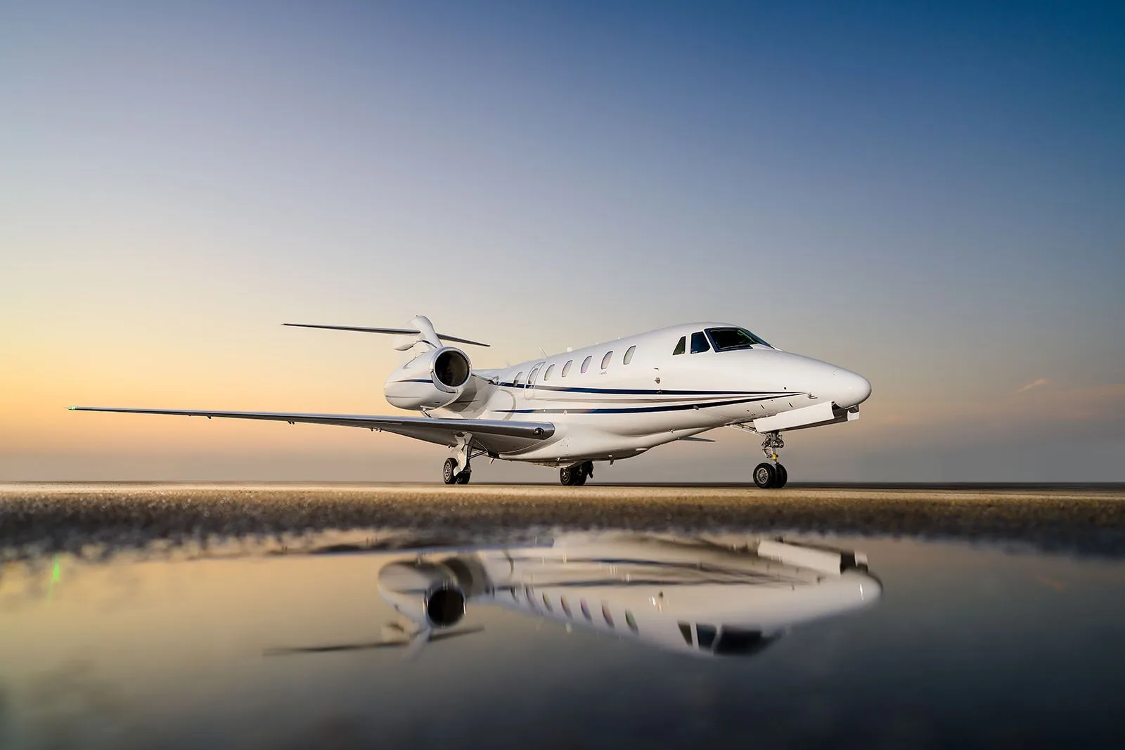 A white jet aircraft parked on the tarmac with a reflection in the water.