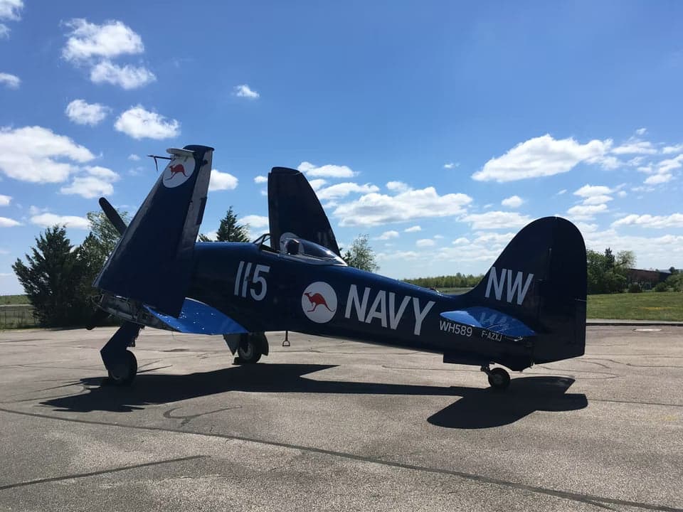 A blue aircraft parked on the tarmac with its wings folded.