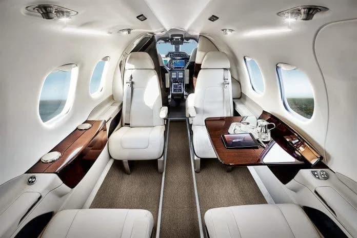 A view of the Phenom 300E cabin with white leather seats and wood accents.
