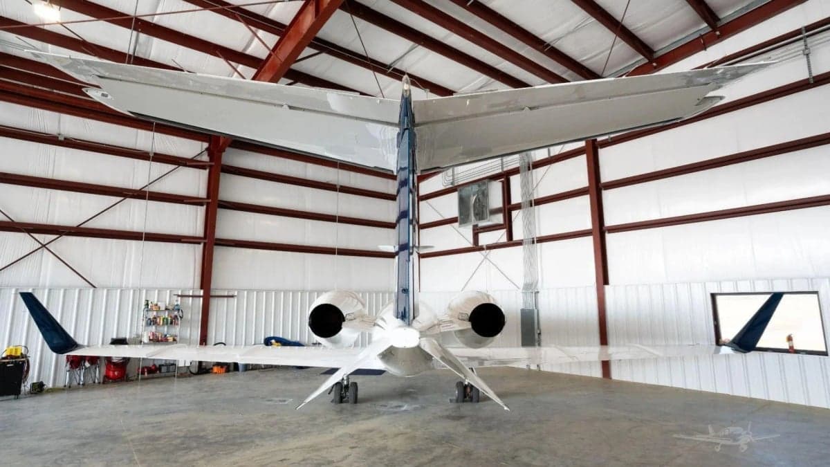Rear view of a white Learjet 31A with blue tail accents, parked inside a hangar.