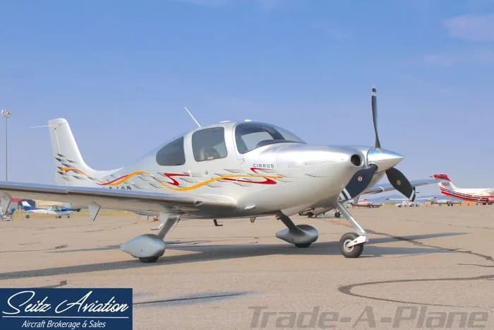 A silver Cirrus aircraft with red and yellow accents parked on the tarmac.