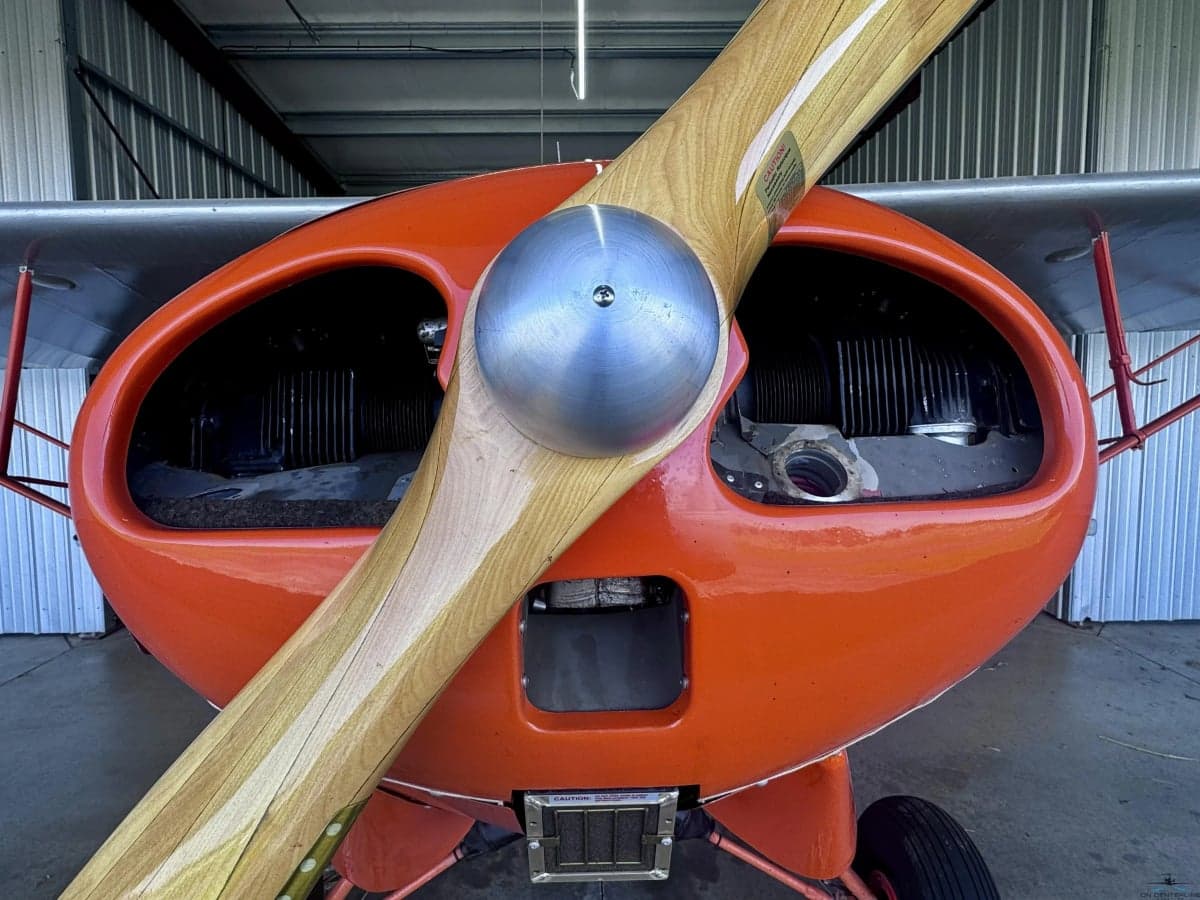 A close-up front view of the wooden propeller and the orange aircraft's engine cowling.