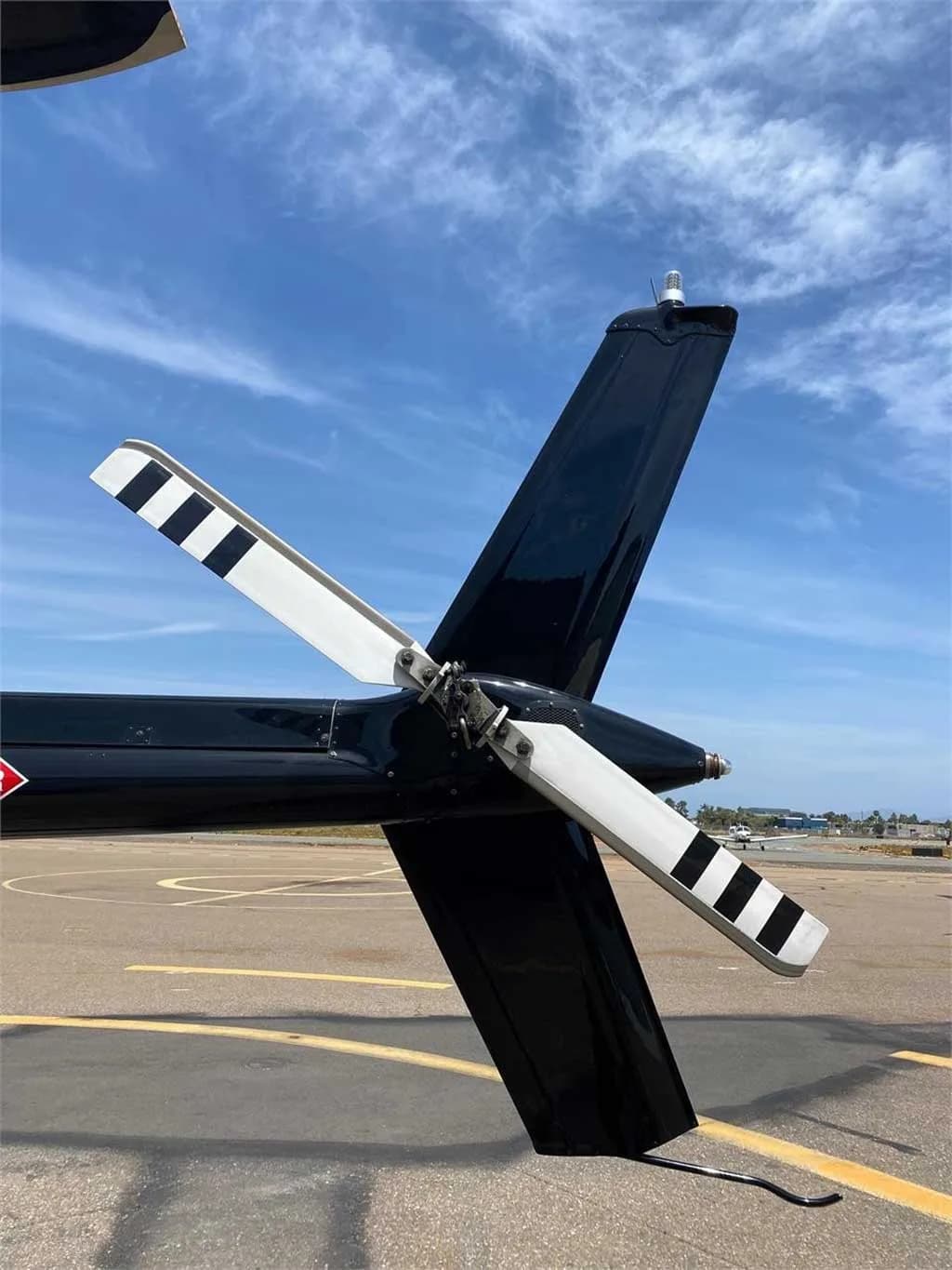 A close-up view of the black tail boom and striped tail rotor of the Bell 206 helicopter on an airfield.