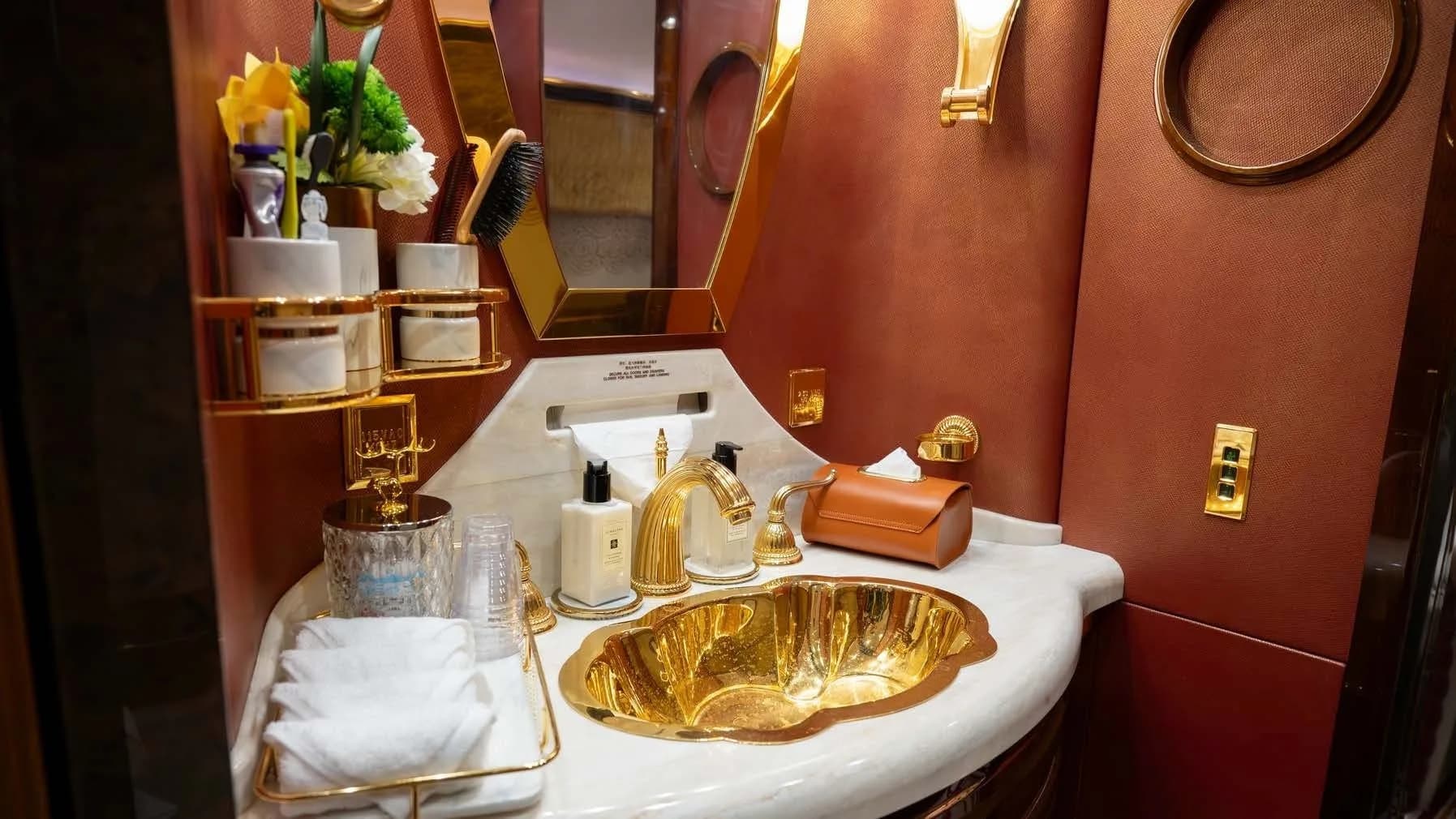 A luxurious aircraft lavatory with a golden sink, marble countertop, and gold-plated fixtures.