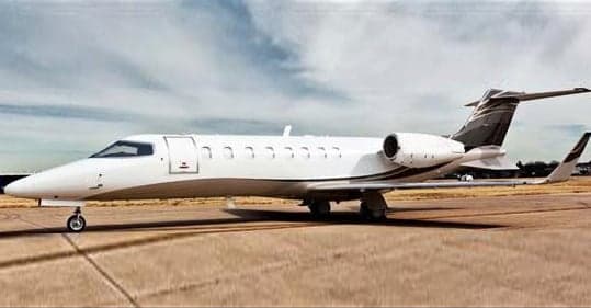 A white and gray Learjet parked on the tarmac.