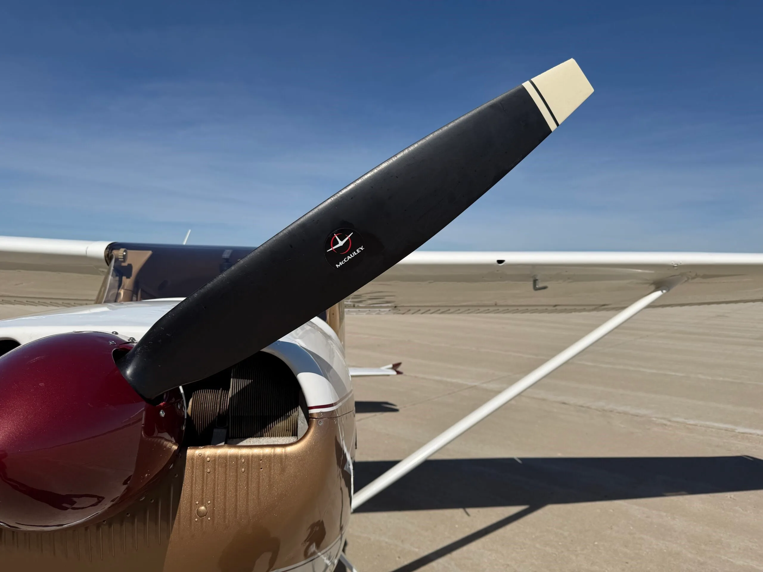 Close-up of the propeller and engine cowling of a white, gold, and maroon Cessna 172.