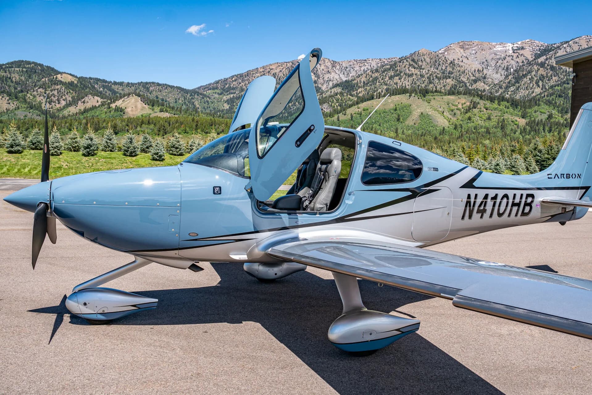 A close-up side view of a light blue and silver Cirrus SR22T aircraft (N410HB) with its doors open.