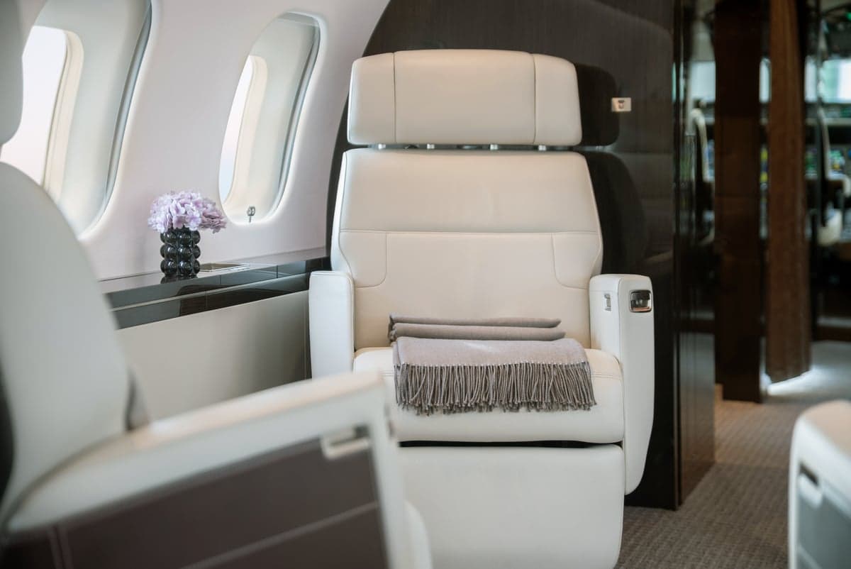 A single white leather seat with a blanket in the aircraft cabin.