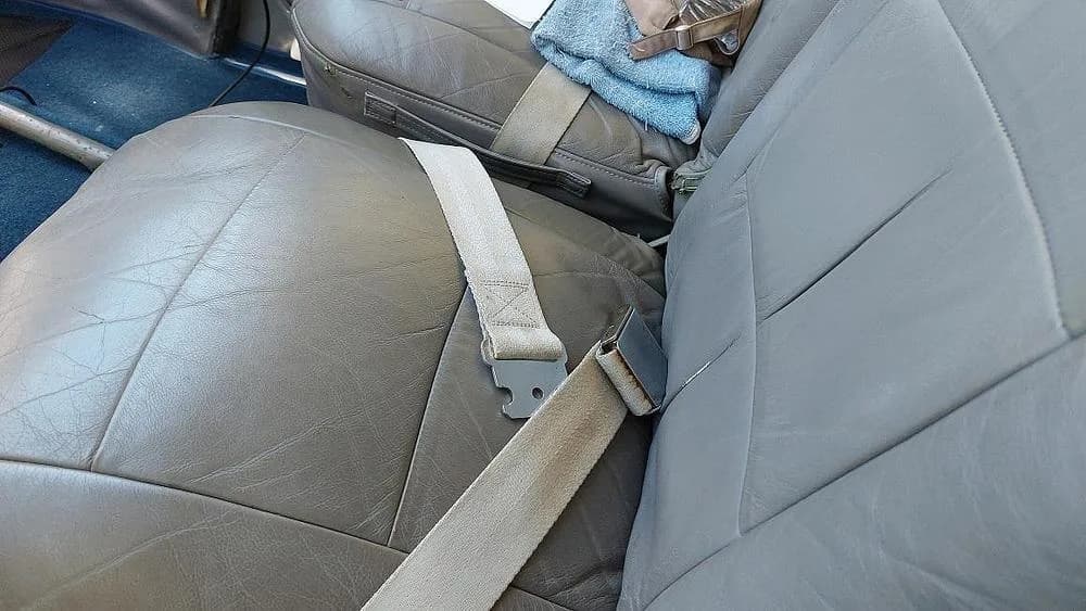 A close-up view of two grey leather aircraft seats with seatbelts inside the cabin.