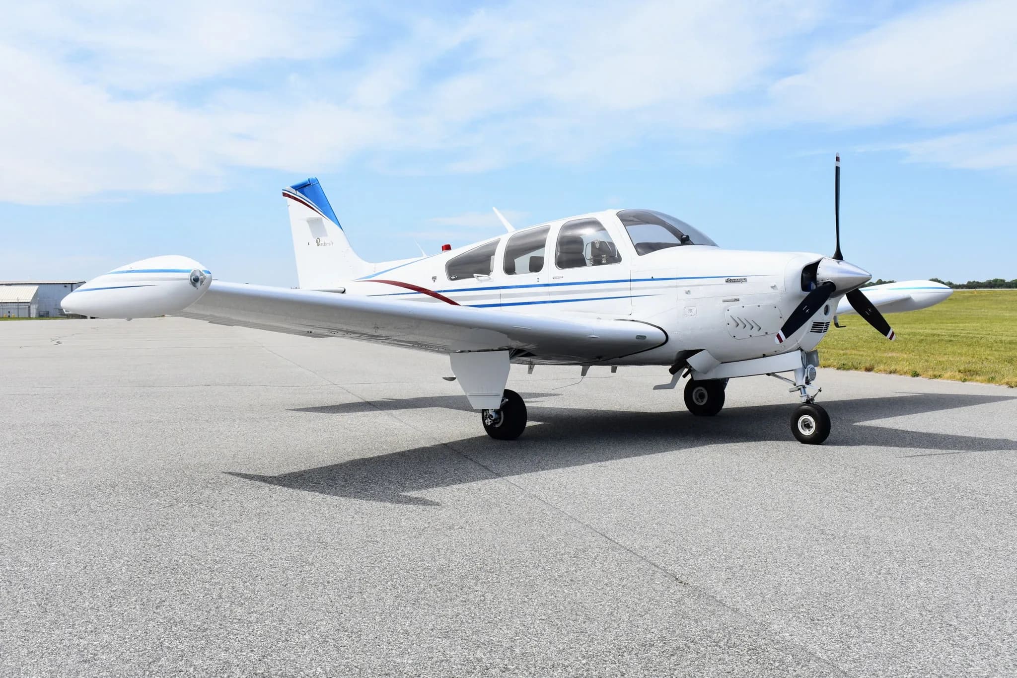 A white Beechcraft Bonanza F33A with blue and maroon stripes, registration N1133A, parked on an asphalt tarmac.