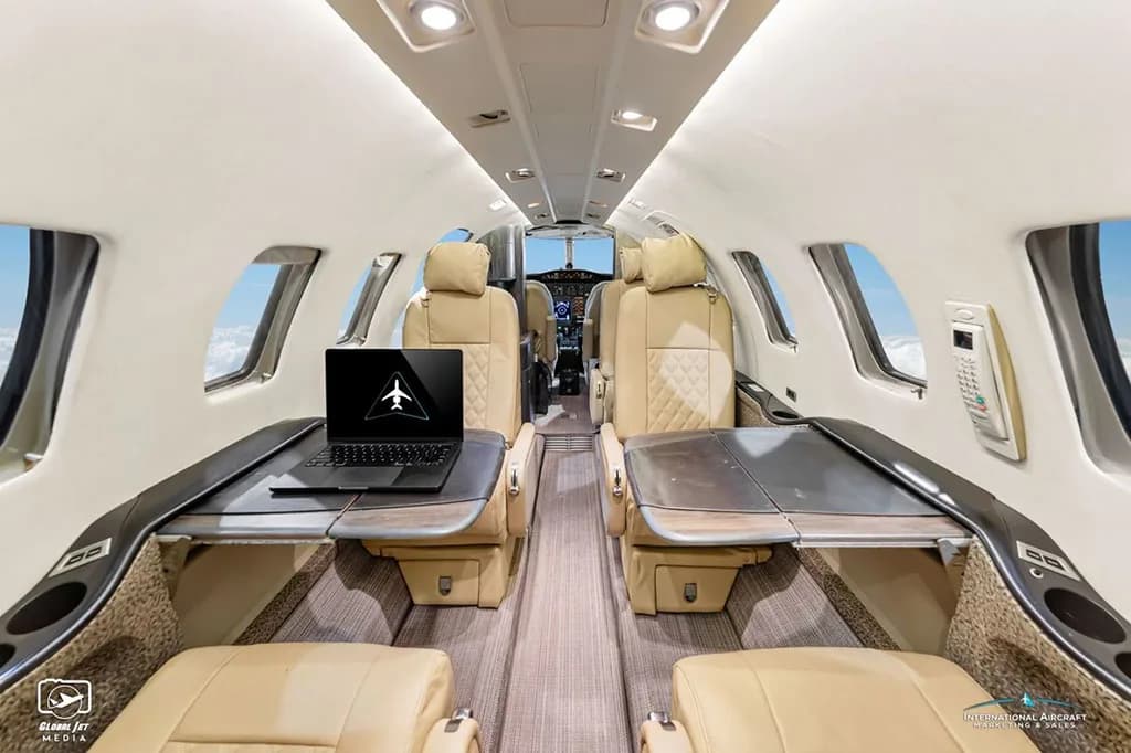 The tan leather interior cabin of a business jet with a laptop on a deployed table.