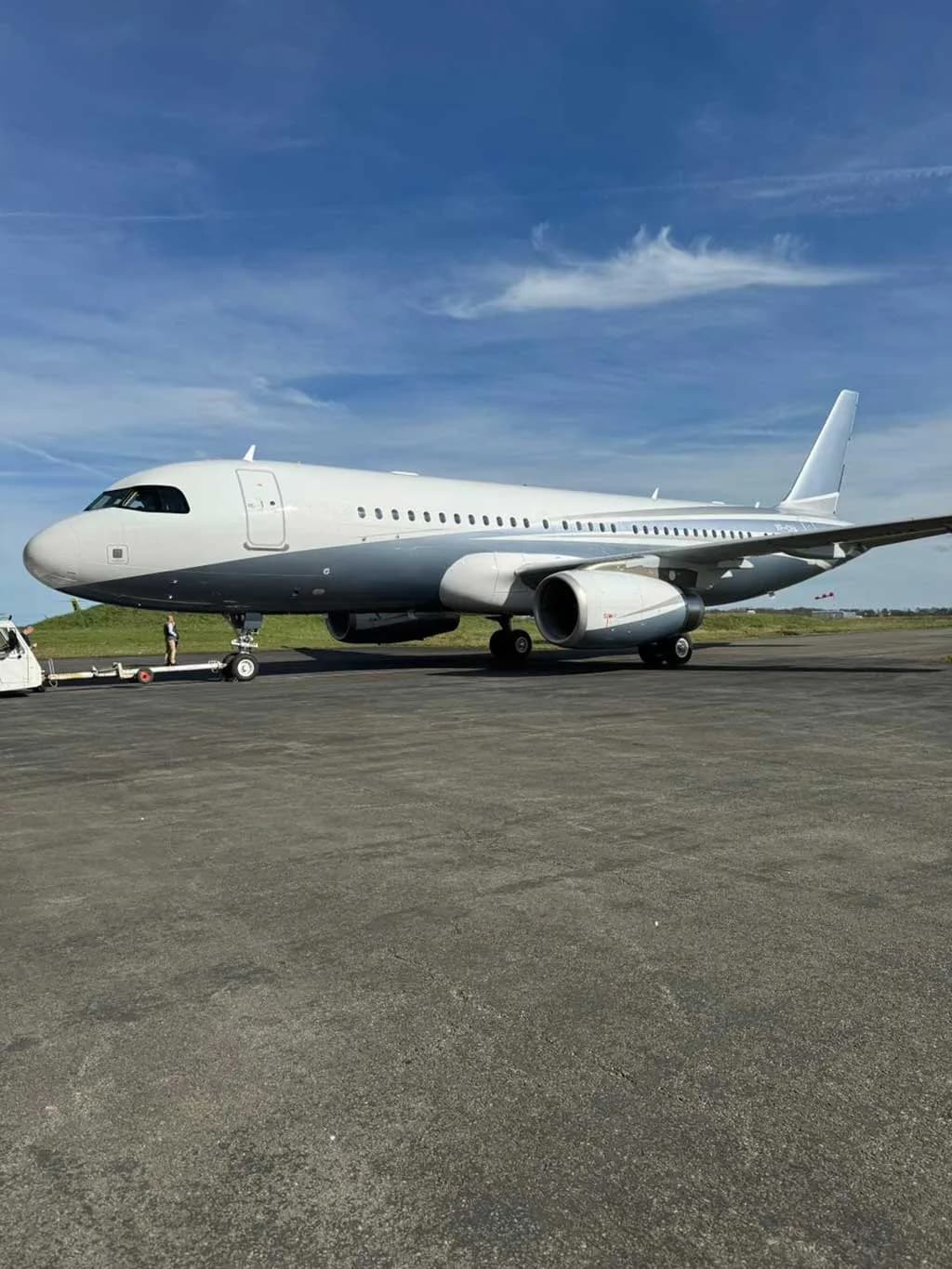 A large white and grey private jet is parked on an asphalt tarmac under a blue sky.