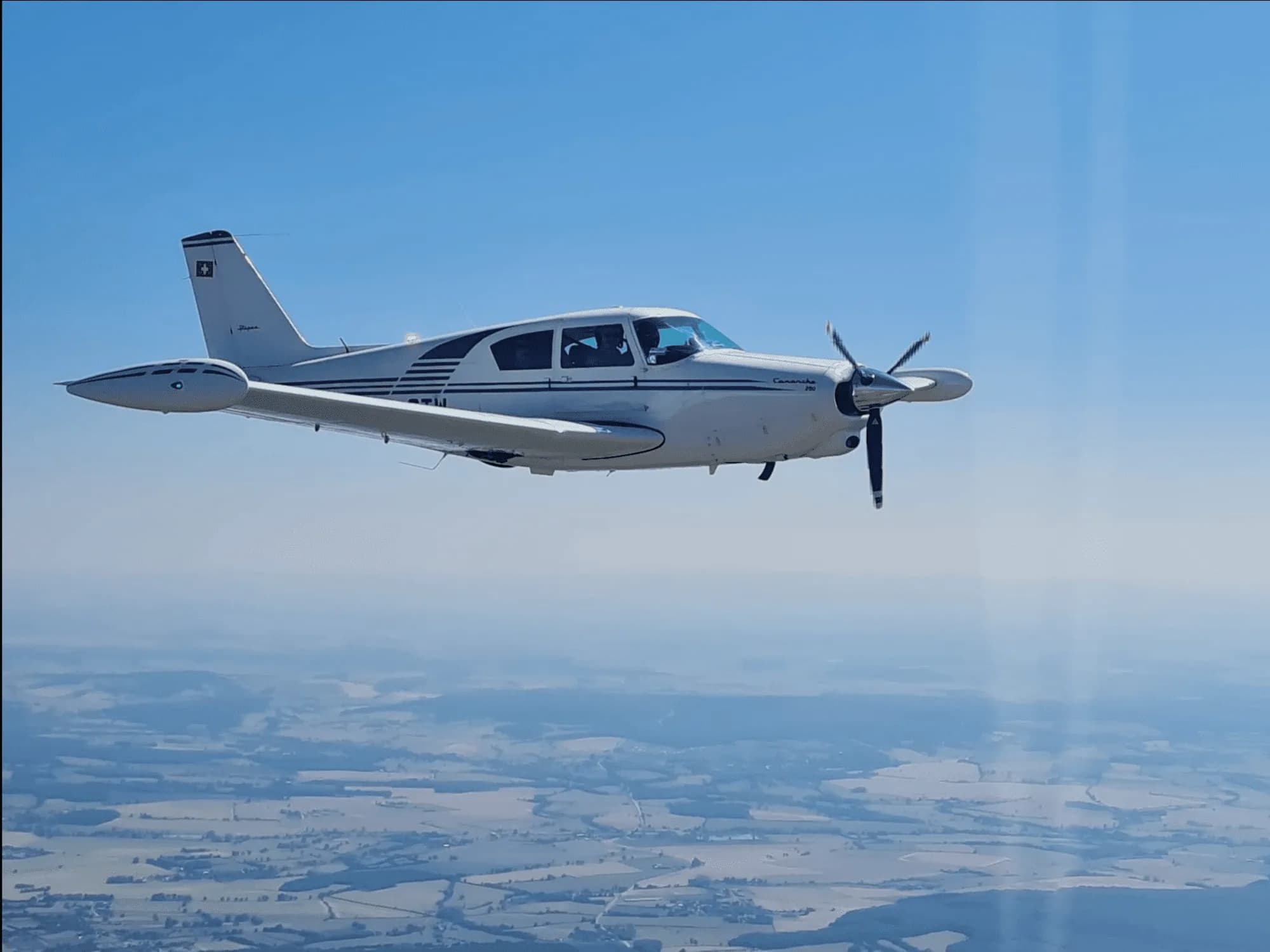 A Piper Comanche 250 in flight against a blue sky.
