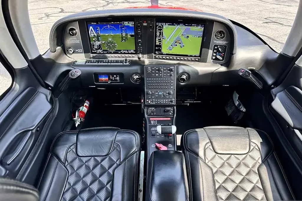 A wide view of the Cirrus SR22 cockpit, showing the instrument panel, control yokes, and front black leather seats.