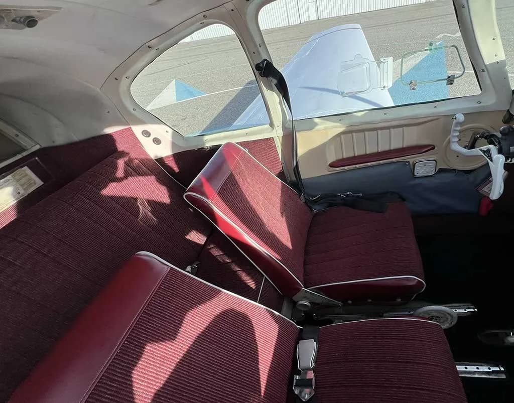 The interior of an aircraft cabin showing two rows of red striped fabric seats.