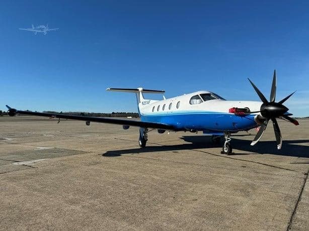 A Pilatus PC-12 aircraft with a blue and white paint scheme is parked on the tarmac.