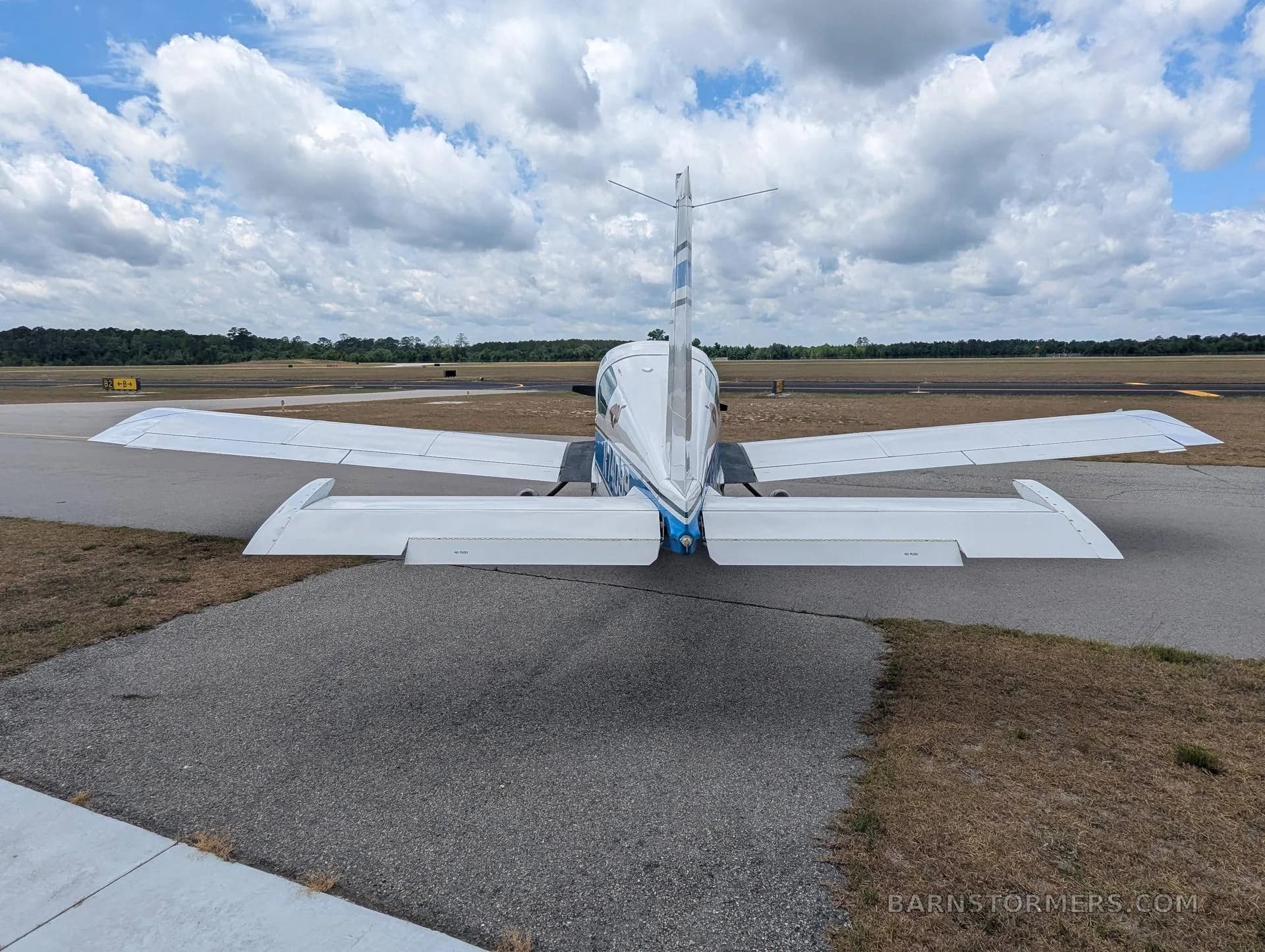A rear view of a white and blue Grumman AA-5 aircraft with registration N74099 parked on an airfield.