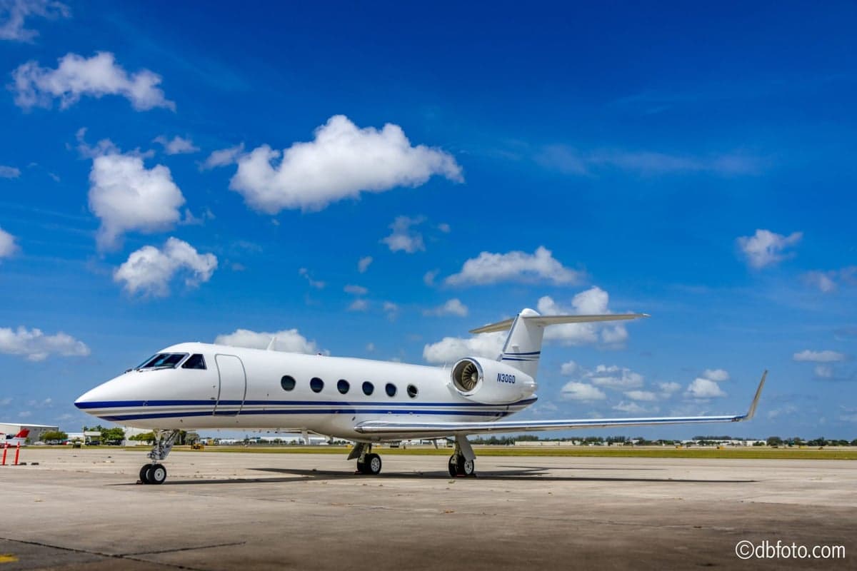 Side view of a white Gulfstream jet with blue stripes on the ramp under a blue sky.